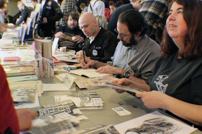 David Lasky signs one of his self-published comics, with his sometimes collaborator Greg Stump in the background. 